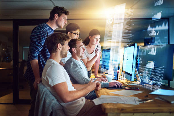 Shot of a group of young people using a computer with a virtual screen during a late night at work